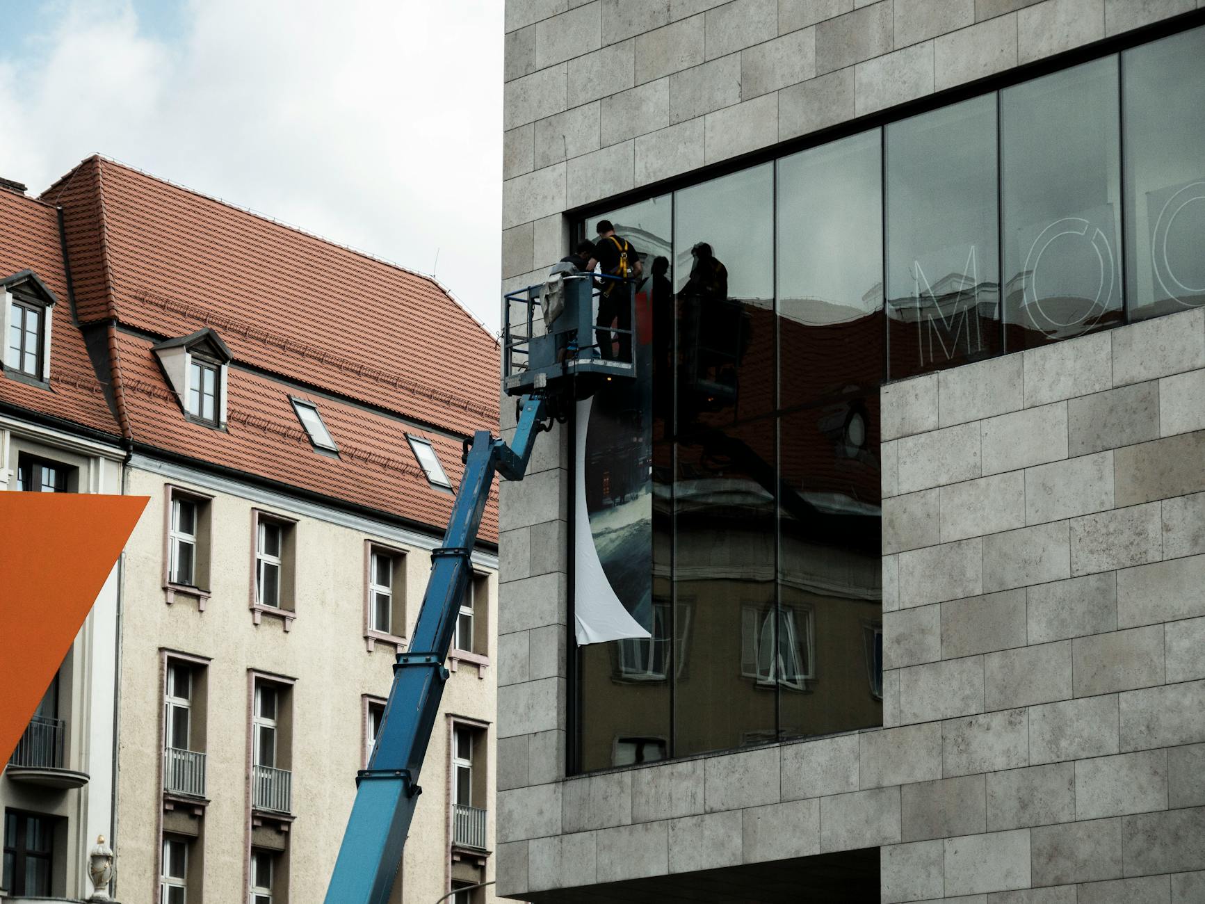 Pracownicy na podnośniku montują wielki baner na szklanym biurowcu