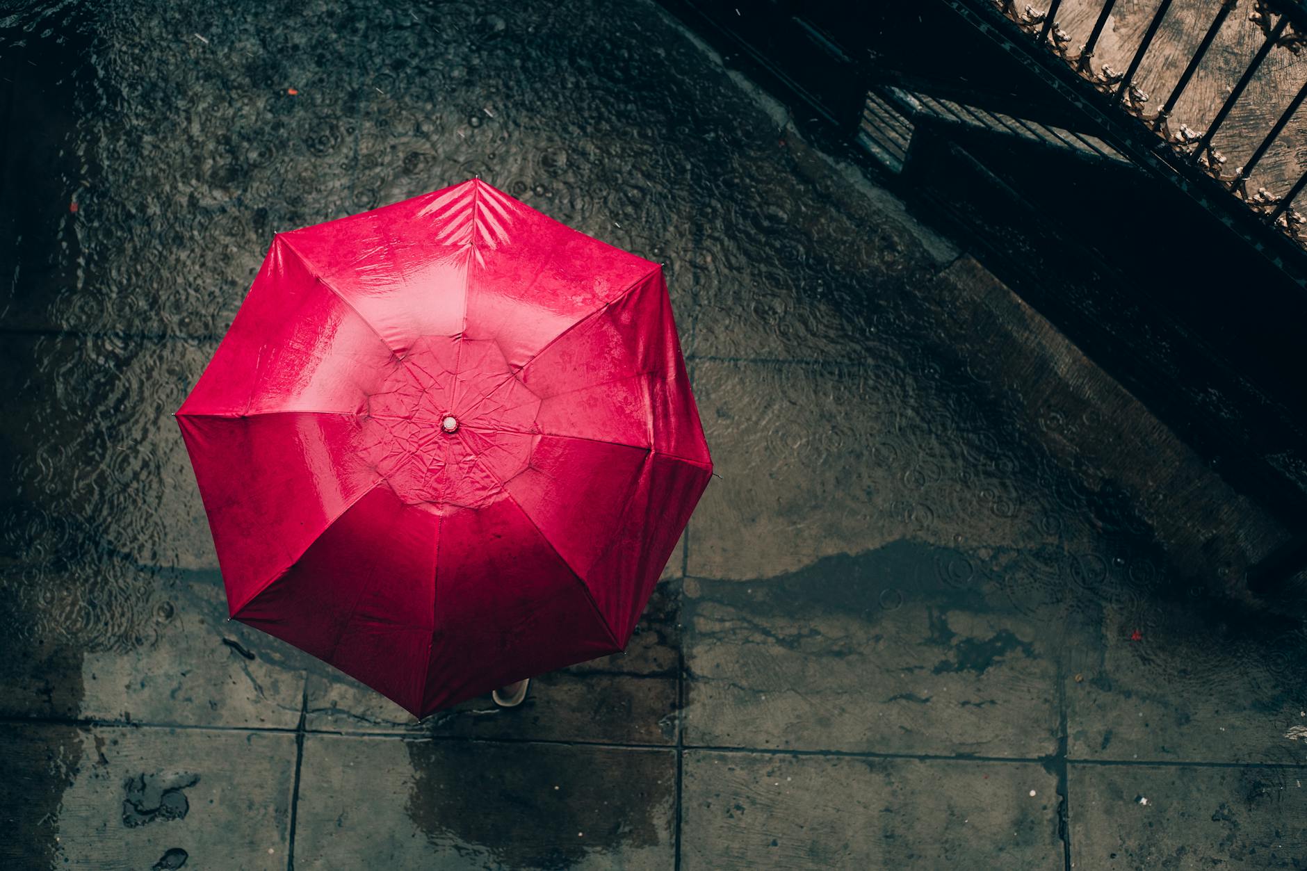 Czerwony parasol z lotu ptaka na mokrej, deszczowej ulicy miasta